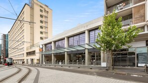 A modern building with a glass entrance and a tram line nearby.