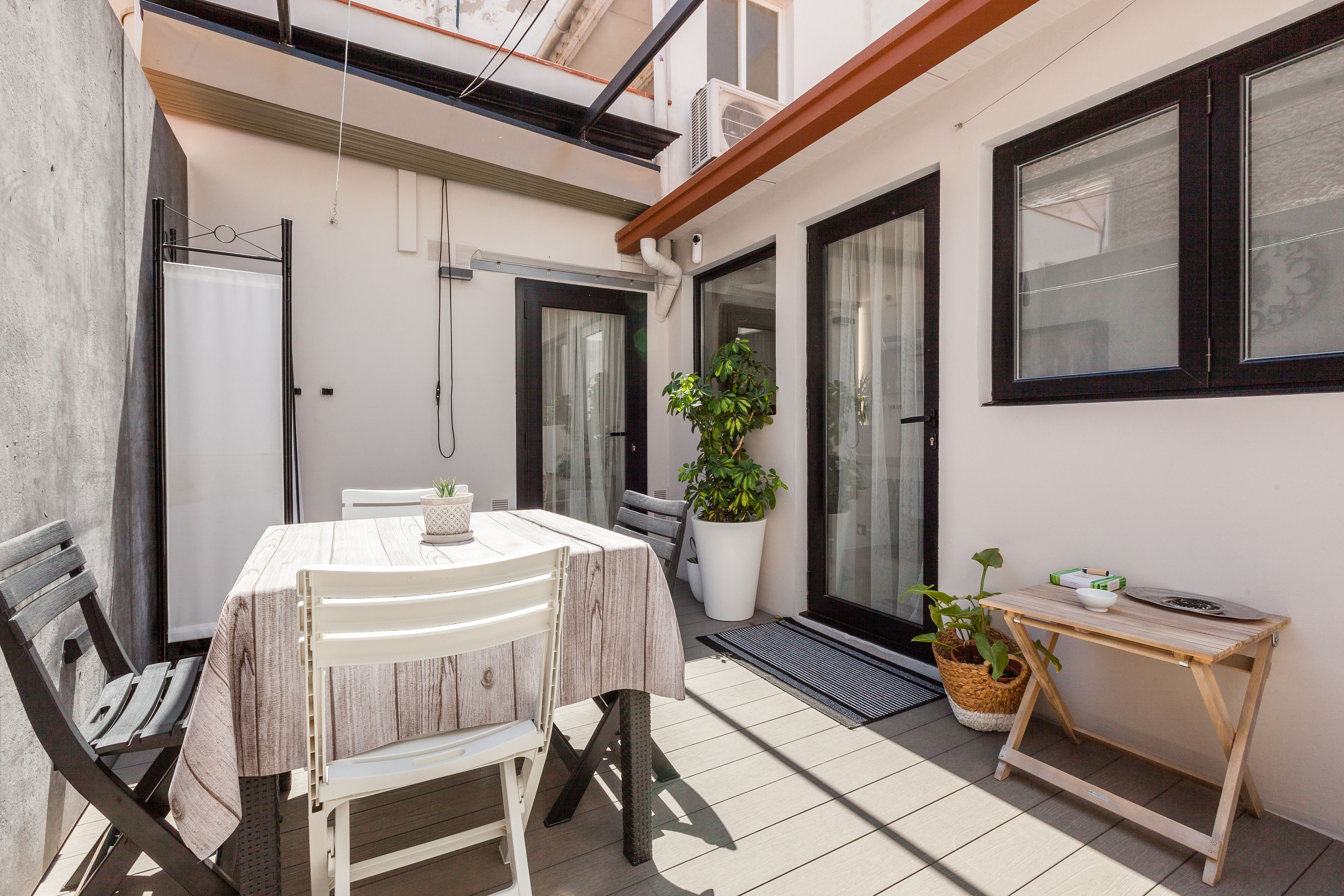 Une terrasse avec une table et des chaises, un pot de fleurs et une petite table en bois sur laquelle se trouvent un bol et un plateau.