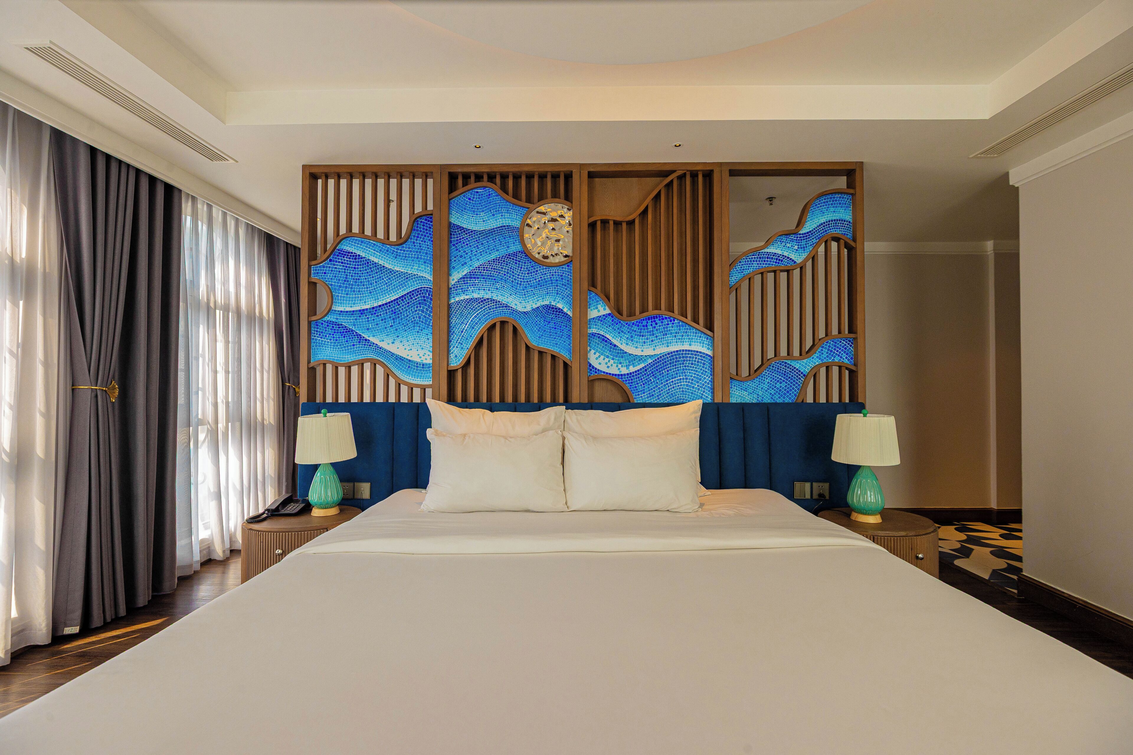 A hotel room with a large bed, two bedside tables, a decorative headboard, and a view of the room's interior.