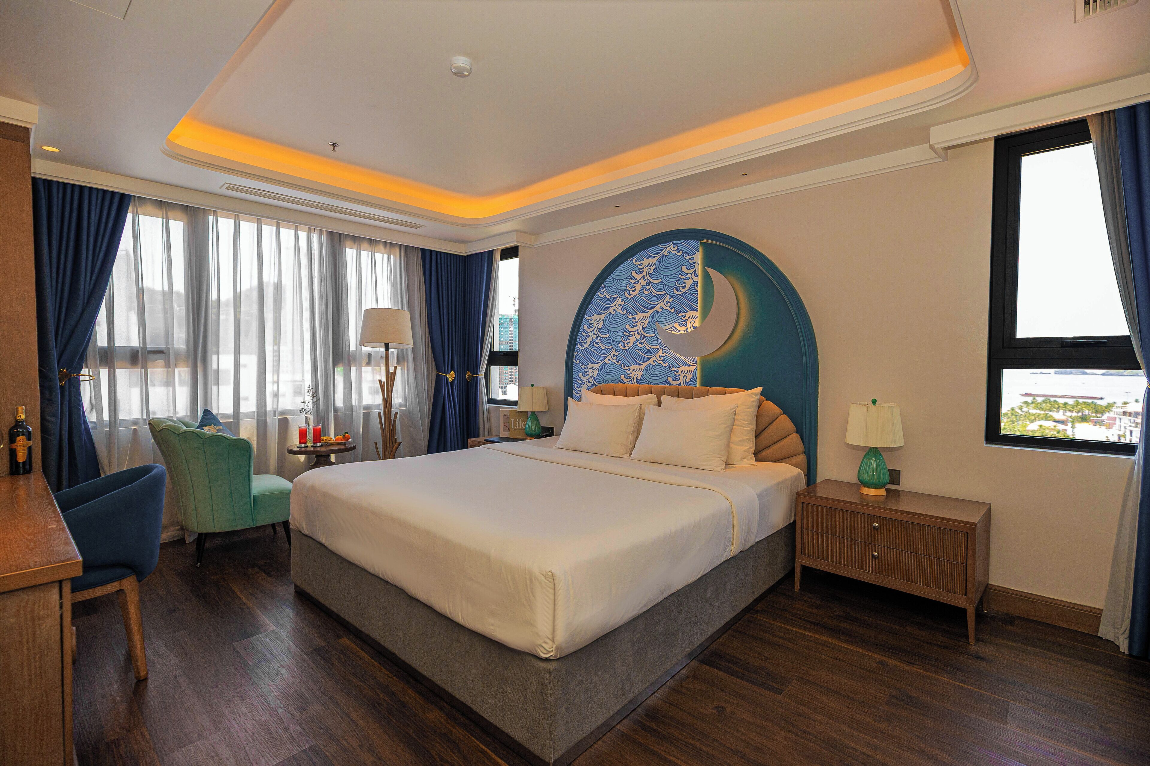 A hotel room with a large bed, a desk, a chair, a nightstand, and a view of the city.