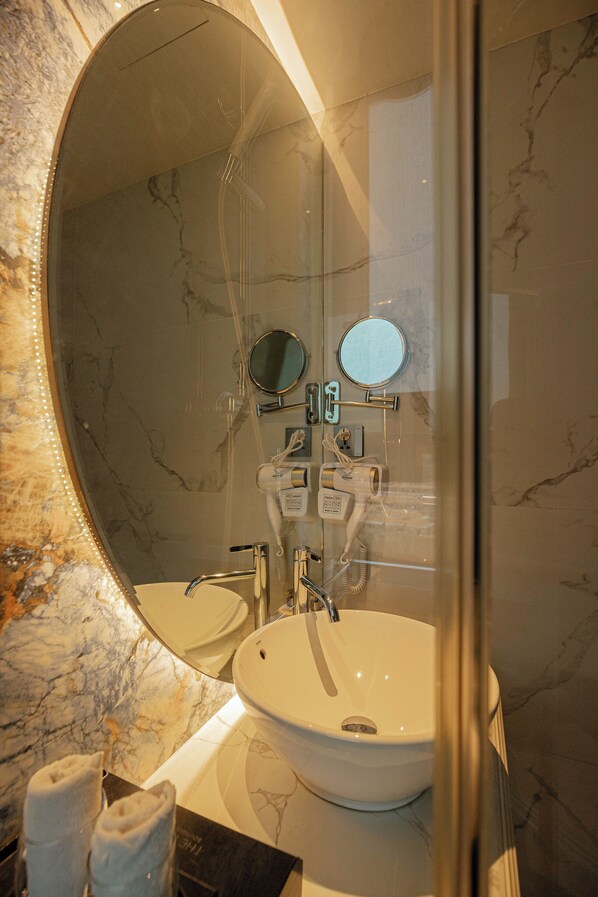 A bathroom with a large oval mirror, two sinks, a towel rack, and a hairdryer.