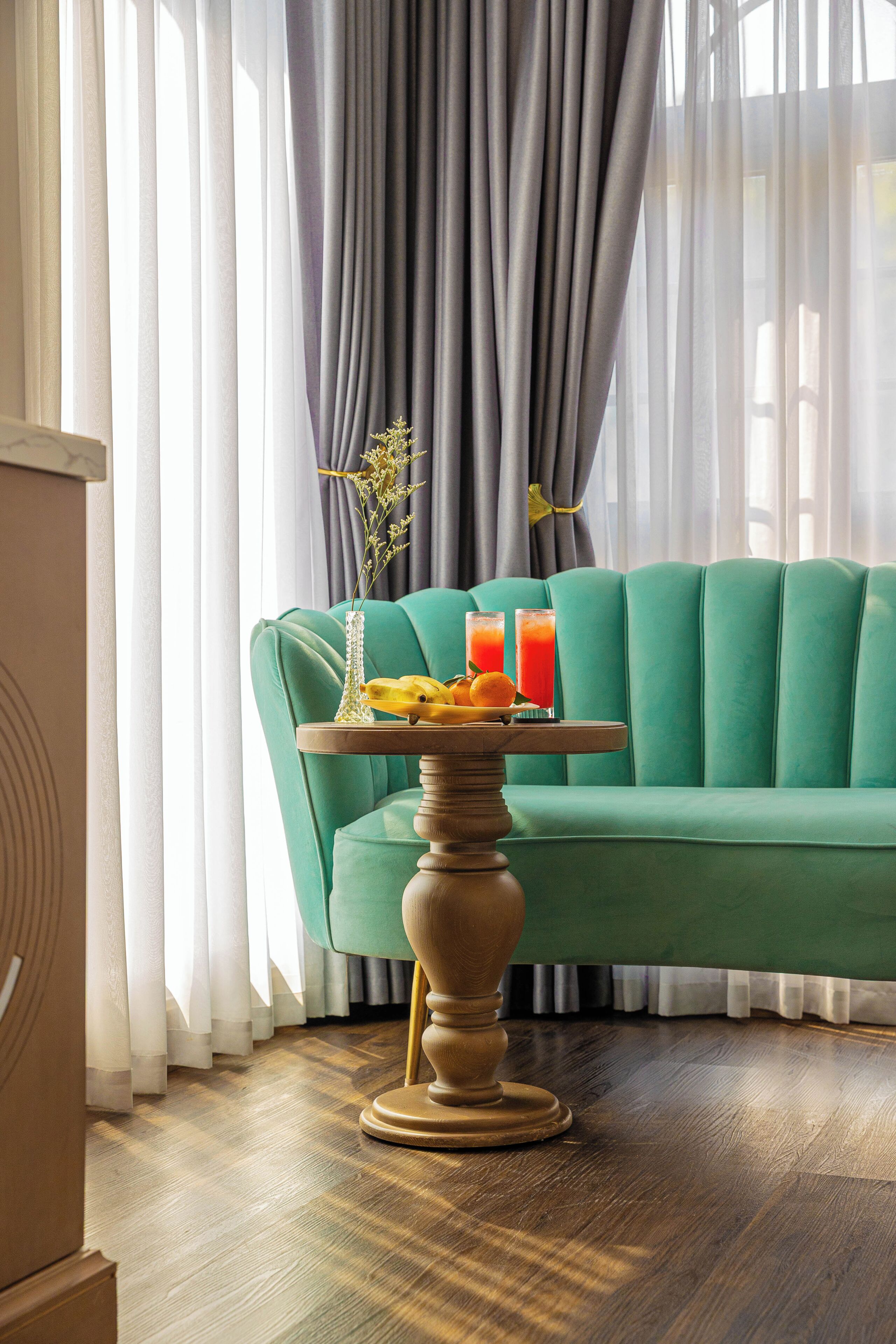 Une pièce avec un canapé de couleur turquoise, une table en bois sur laquelle se trouve un plateau de fruits et de boissons, et un vase rempli de fleurs.
