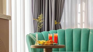 A room with a teal sofa, a wooden table with a tray of fruit and drinks, and a vase with flowers.