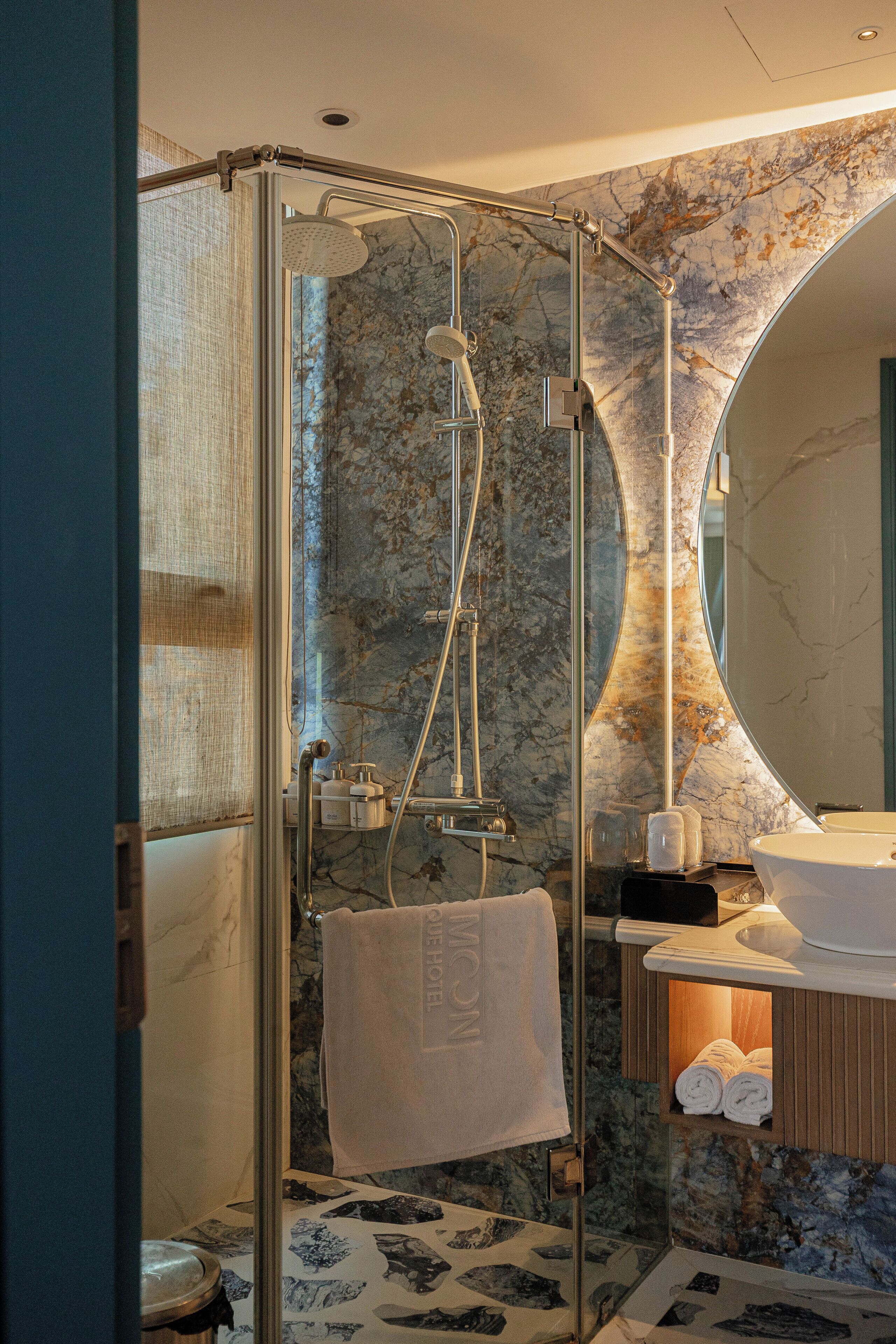 A modern bathroom with a glass-enclosed shower, marble walls, and a large mirror.