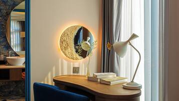 A modern room with a round mirror, a desk with a lamp, and a blue chair.