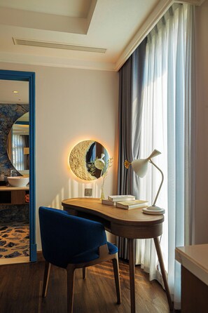 A modern room with a round mirror, a desk with a lamp, and a blue chair. - The Moon Boutique Hotel Cat Ba (Hai Phong)