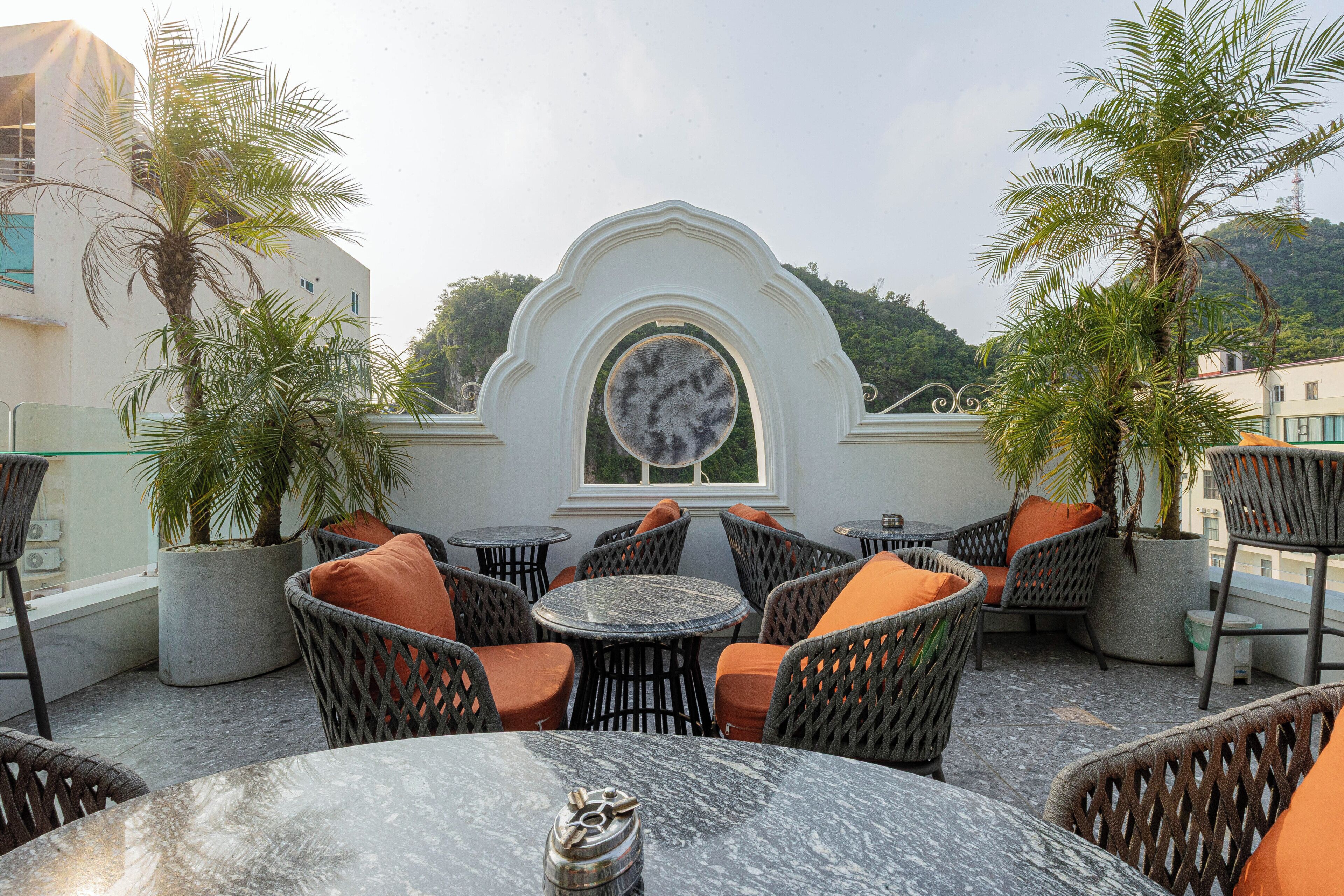 An outdoor seating area with wicker chairs and tables, a decorative archway, and potted plants.