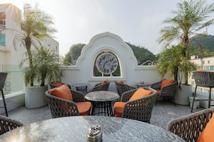 An outdoor seating area with wicker chairs and tables, a decorative archway, and potted plants.