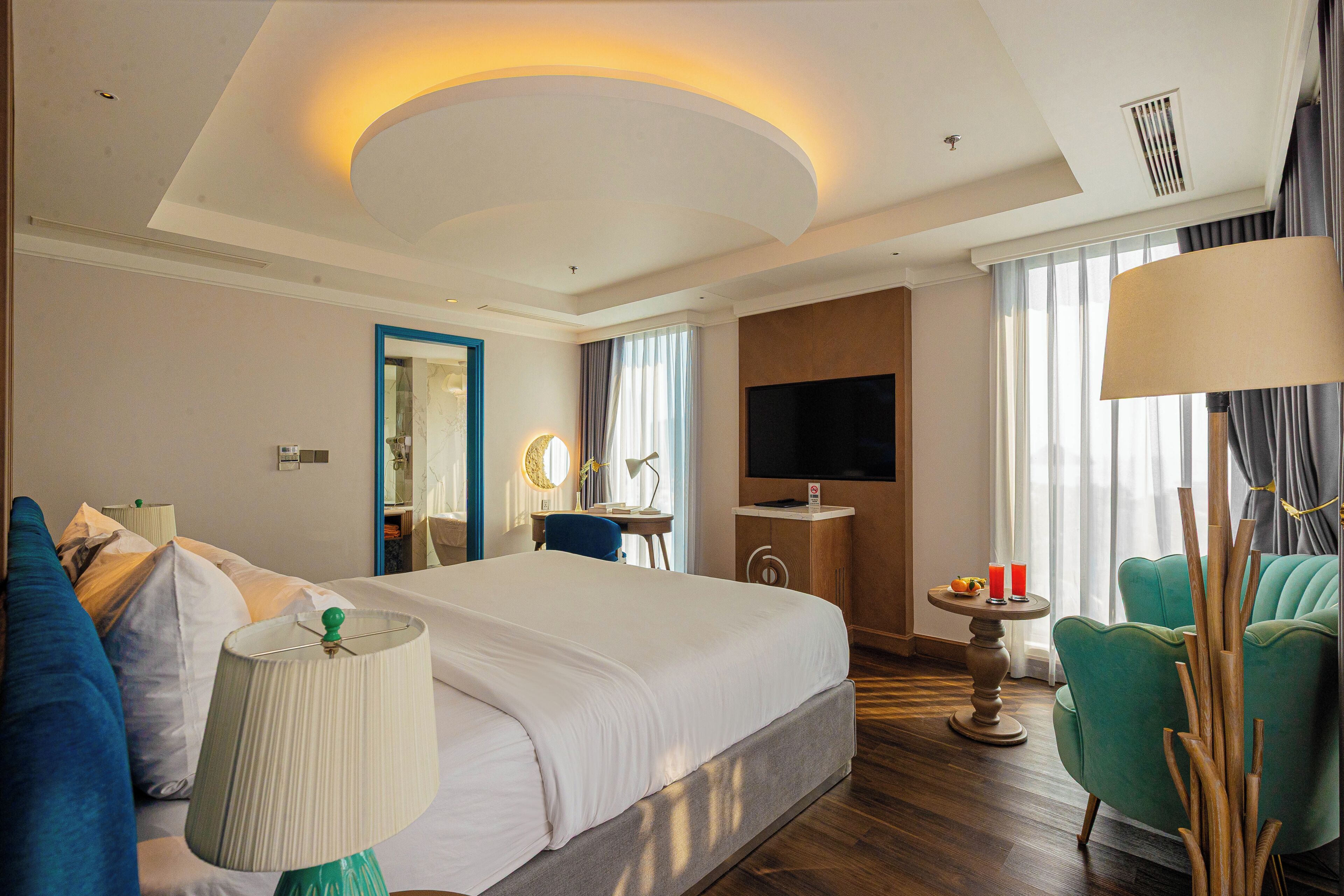 A hotel room with a large bed, a desk, a TV, and a seating area with a chair and a table.
