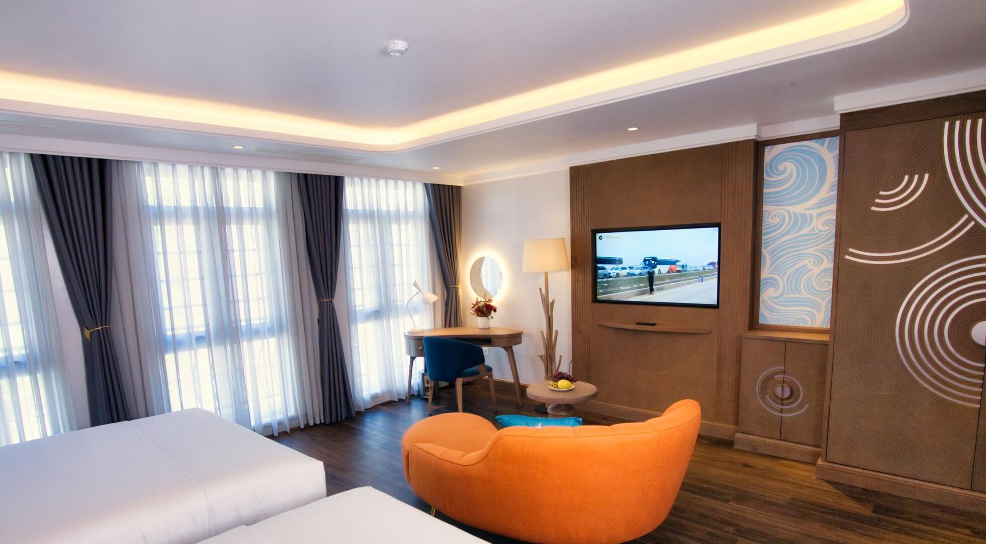 A hotel room with a bed, a desk with a chair, a television, and a decorative wall panel.