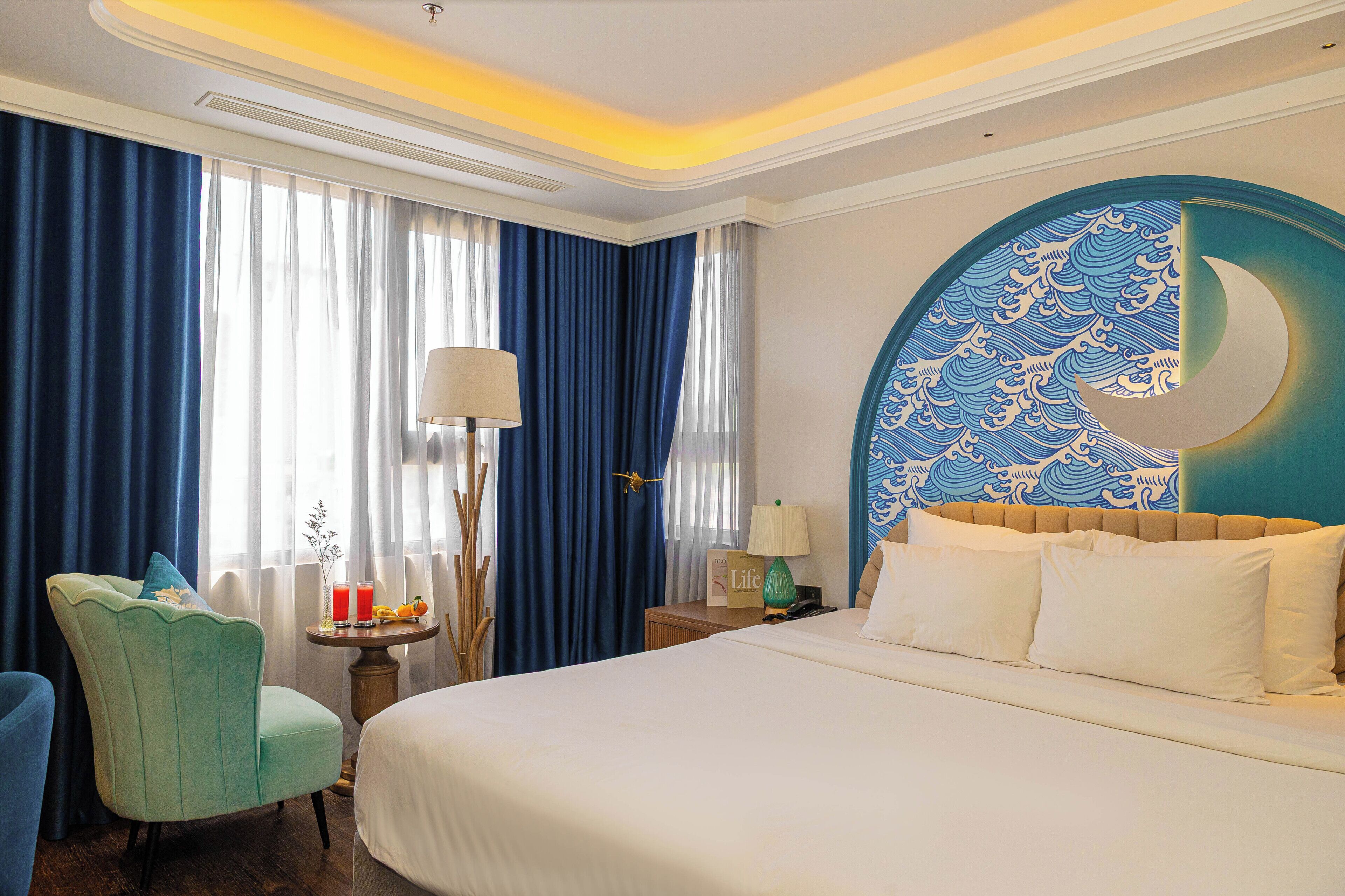 A hotel room with a large bed, a desk with a lamp, a chair, and a wall with a decorative crescent moon design.