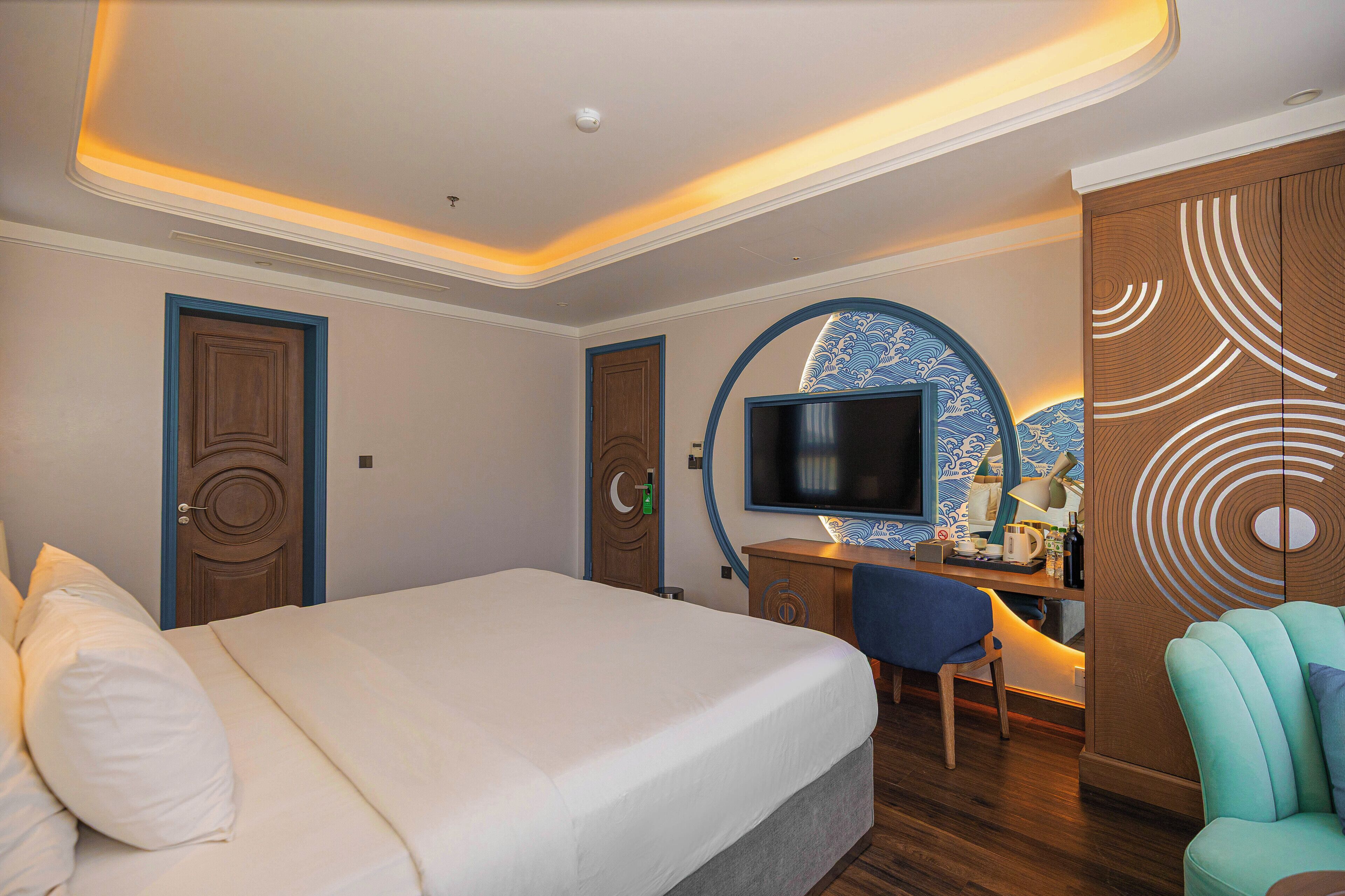 A hotel room with a bed, desk, chair, television, and a decorative wall.