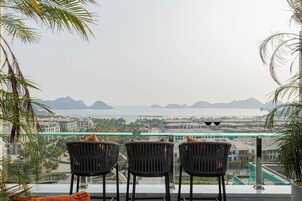 A balcony with two chairs facing a view of a coastal cityscape, including buildings and mountains.
