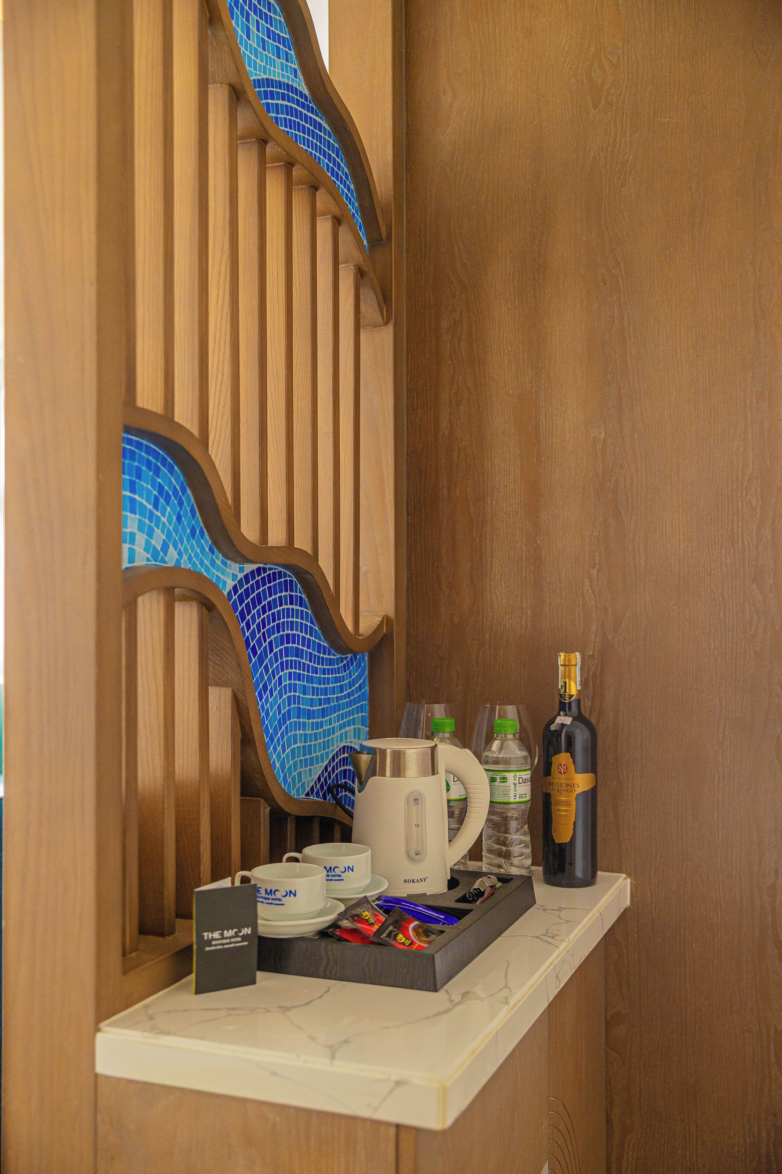 Eine Holzvertäfelung mit blauem Mosaikmuster, eine Marmorarbeitsplatte mit Kaffeemaschine, Tassen, einer Weinflasche und einer Minibar mit Snacks.
