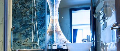 Une salle de bain moderne dotée d’une douche à parois de verre, de murs en marbre, d’un grand miroir et d’un lavabo en forme de vasque.