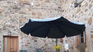Ein Steingebäude mit einer Holztür, einem Tisch mit St ühlen und einem Sonnenschirm.