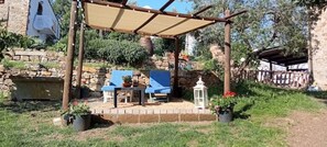 Un área de estar al aire libre techada con un muro de piedra, una mesa, sillas y plantas en macetas.