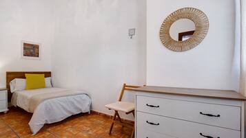 Un dormitorio con cama, sillón, cómoda, espejo en la pared y un cuadro.
