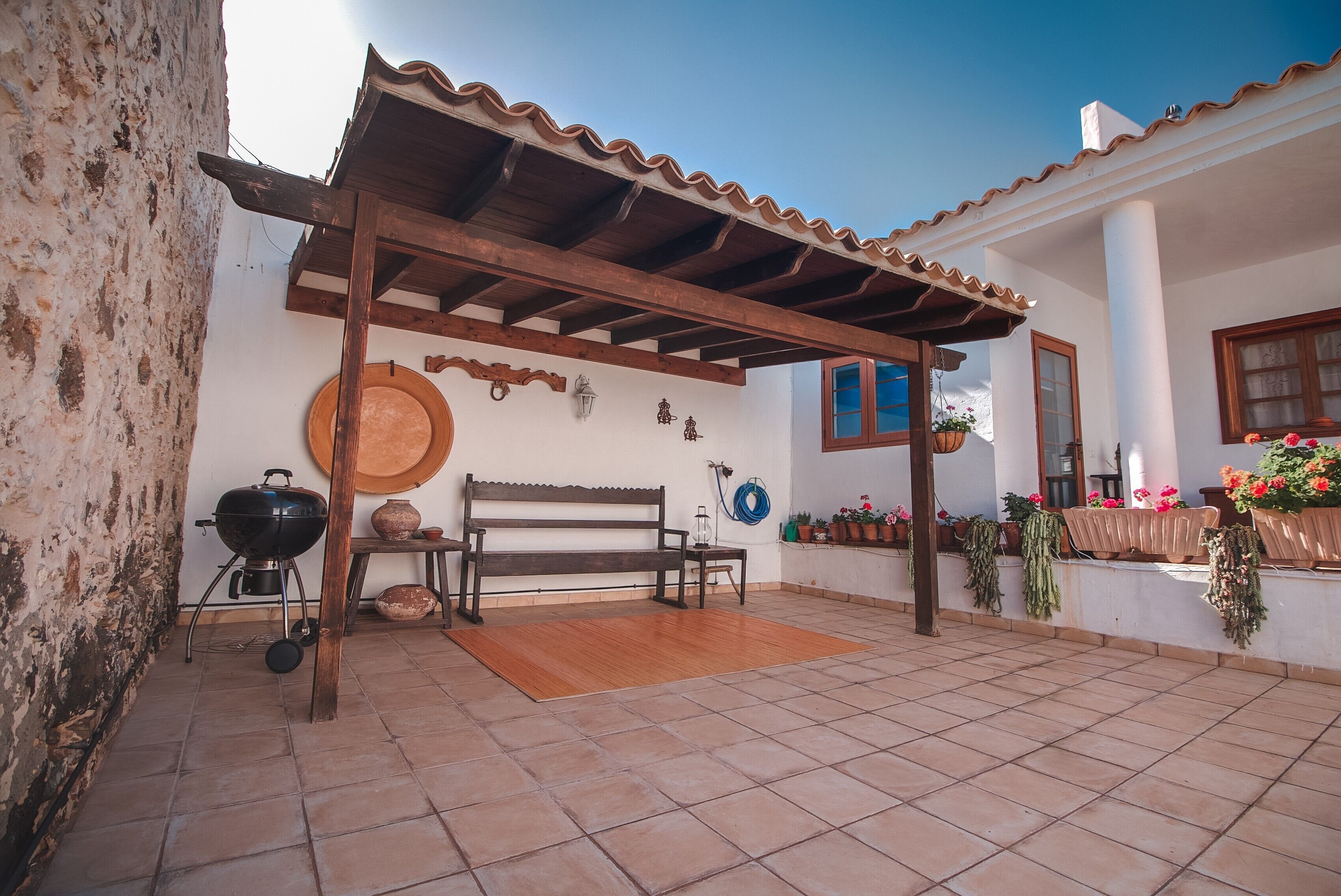 Un patio techado con un banco de madera, una parrilla y plantas en macetas.