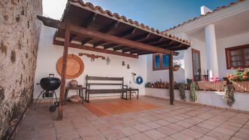 Un patio techado con un banco de madera, una parrilla y plantas en macetas.