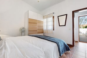Un dormitorio con cama, armario, ventilador y espejo, y vistas al exterior.
