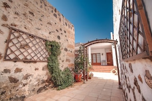 Un estrecho callejón con una pared de piedra rústica, un portón de madera y una planta en maceta.