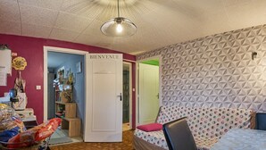 Ein Zimmer mit einem 'BIENVENUE'-Schild, einer Wand mit Muster, einem Bett mit farbigem Kissen und einem Tisch mit Taschen.