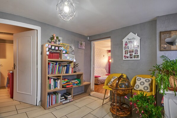 Une pièce avec une bibliothèque, un globe terrestre, un fauteuil jaune et un mur décoré de photos de famille.