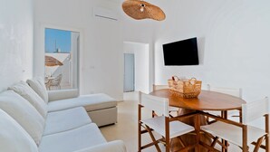Un salon moderne comprenant un canapé, une table à manger, des chaises, un téléviseur et un panier en osier.