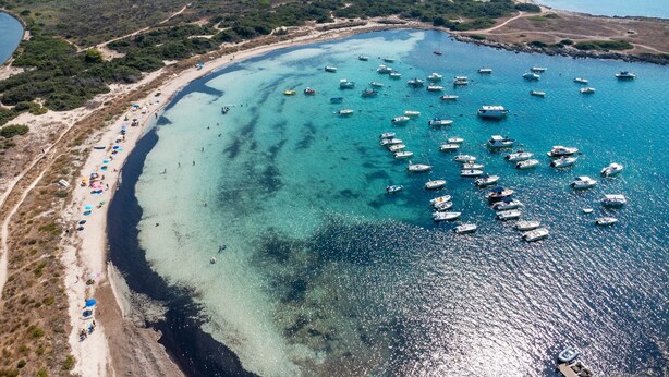 Vue aérienne d’une zone côtière avec une plage, des bateaux et une eau cristalline.