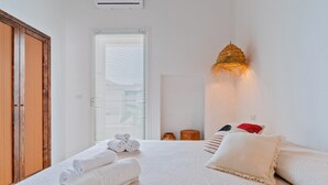 Une chambre à coucher avec un lit, des serviettes enroulées, un luminaire fixé au mur et une fenêtre avec des stores.