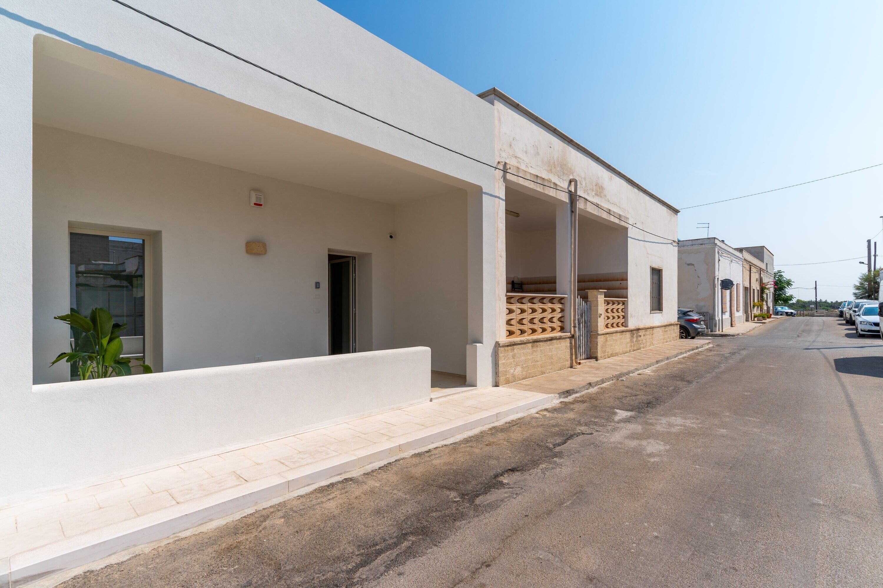 A building with a white facade, a covered outdoor area, and a street with parked cars.