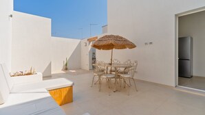 Une terrasse extérieure moderne, dotée d’une table à manger, de chaises, d’un parasol en chaume et d’un canapé blanc.