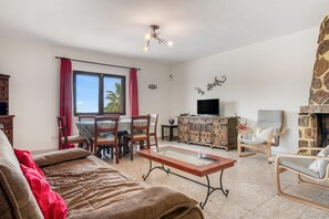 A living room with a sofa, a coffee table, a TV, a fireplace, and a dining area with chairs and a table. - Villa 'Khiter' with Private Pool, Wi-Fi and Air Conditioning (Dénia)