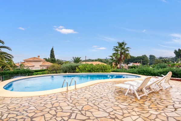 A swimming pool with lounge chairs, surrounded by stone tiles and greenery. - Villa 'Khiter' with Private Pool, Wi-Fi and Air Conditioning (Dénia)