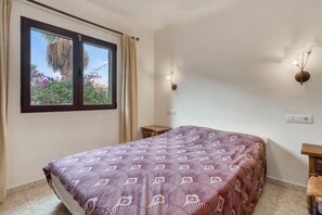 A bedroom with a bed, a window with curtains, a small table, and a wall-mounted light fixture. - Villa 'Khiter' with Private Pool, Wi-Fi and Air Conditioning (Dénia)