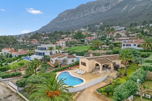 A residential area with a swimming pool, houses with red-tiled roofs, and a mountain in the background. - Villa 'Khiter' with Private Pool, Wi-Fi and Air Conditioning (Dénia)