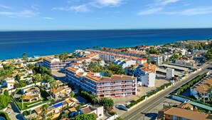 Ett bostadsområde vid kusten med en markant, högre byggnad, en klarblå himmel och havet i bakgrunden.