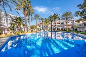 Une piscine entourée de palmiers et de bâtiments blancs dotés de balcons.