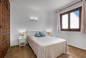 Un dormitorio con cama, mesitas de noche, una ventana y una puerta de madera.