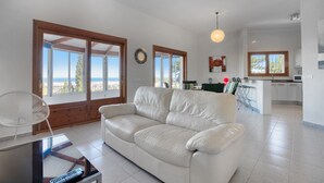 A living room with a white leather sofa, a glass coffee table, and a view of the sea through large windows. - Villa 'Alta' with Private Pool, Wi-Fi and Air Conditioning (Dénia)