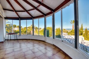 A spacious room with large windows, a tiled floor, and a wooden ceiling structure.