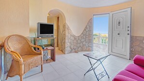 Una stanza con una sedia in vimini, un tavolino, un televisore e una porta che dà su un balcone.
