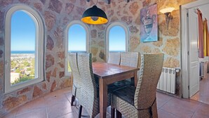 Una stanza dalle pareti in pietra con un tavolo e sedie in legno, ampie finestre ad arco, una lampada a sospensione e un quadro.
