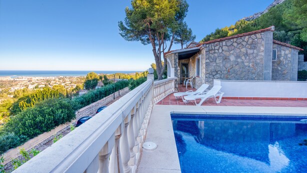 Una piscina con vista sul mare, un edificio in pietra con tetto rosso e un albero sul balcone.