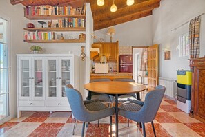 A dining area with a round table, four chairs, a cabinet with glass doors, and a kitchen in the background.