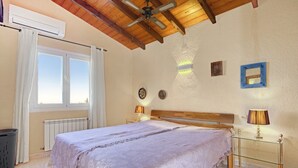 A bedroom with a bed, two bedside lamps, a ceiling fan, a window with curtains, and a radiator. - Villa 'Nicoll' with Private Pool, Wi-Fi and Air Conditioning (Dénia)
