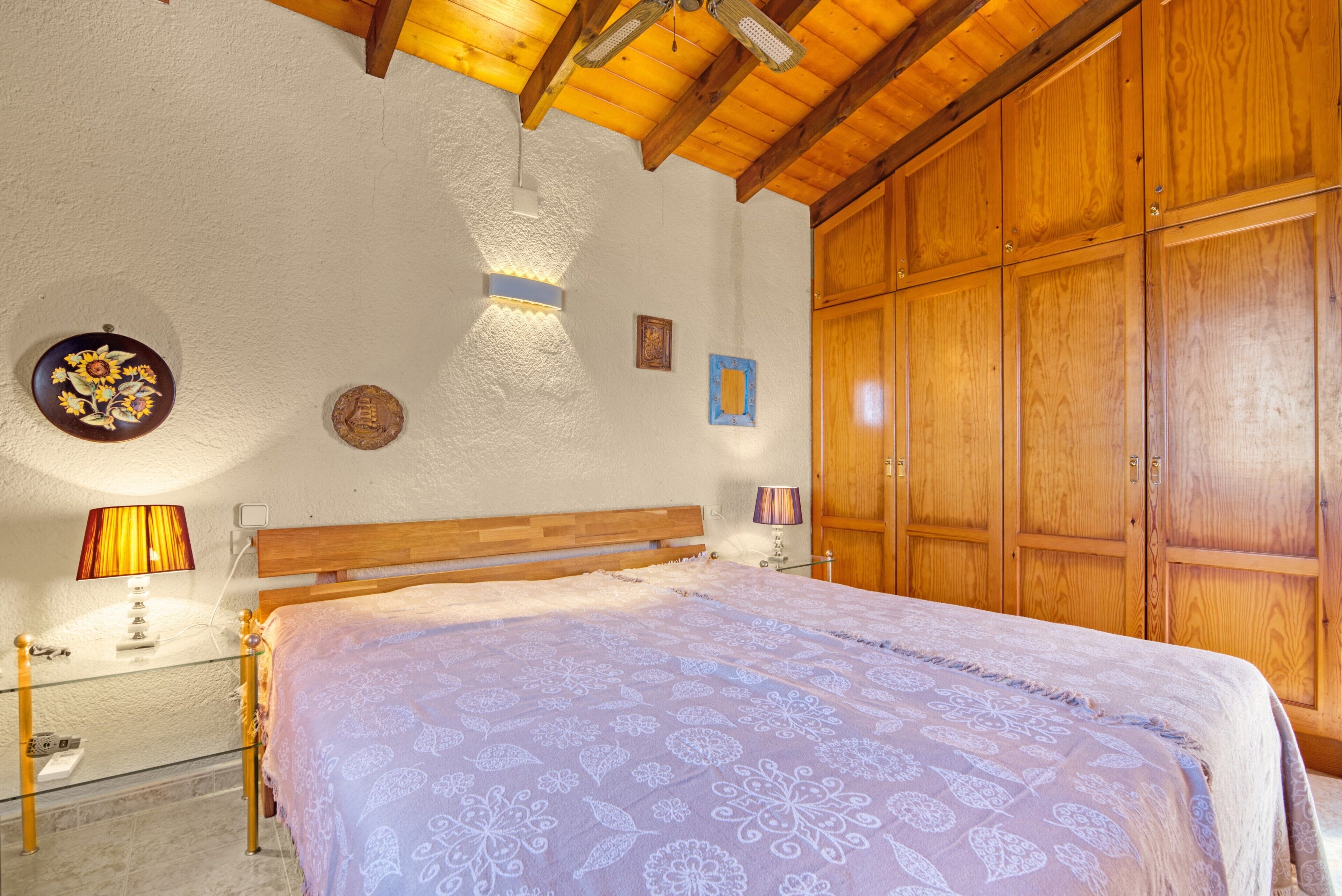 A bedroom with a wooden bed, a nightstand, a lamp, a wall-mounted light fixture, and a wardrobe.