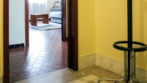 A hallway with a coat rack, a wooden door leading to a room with a bed and a window, and a tiled floor. - Apartment "Semia" with Mountain View, Balcony & Wi-Fi (Vinadio)
