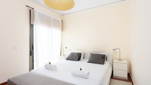 A hotel room with a bed, bedside tables, a lamp, a window with curtains, and a door. - Vacation Home "La Tejita Beach House" with Mountain View, Shared Pool & Wi-Fi (La Tejita)